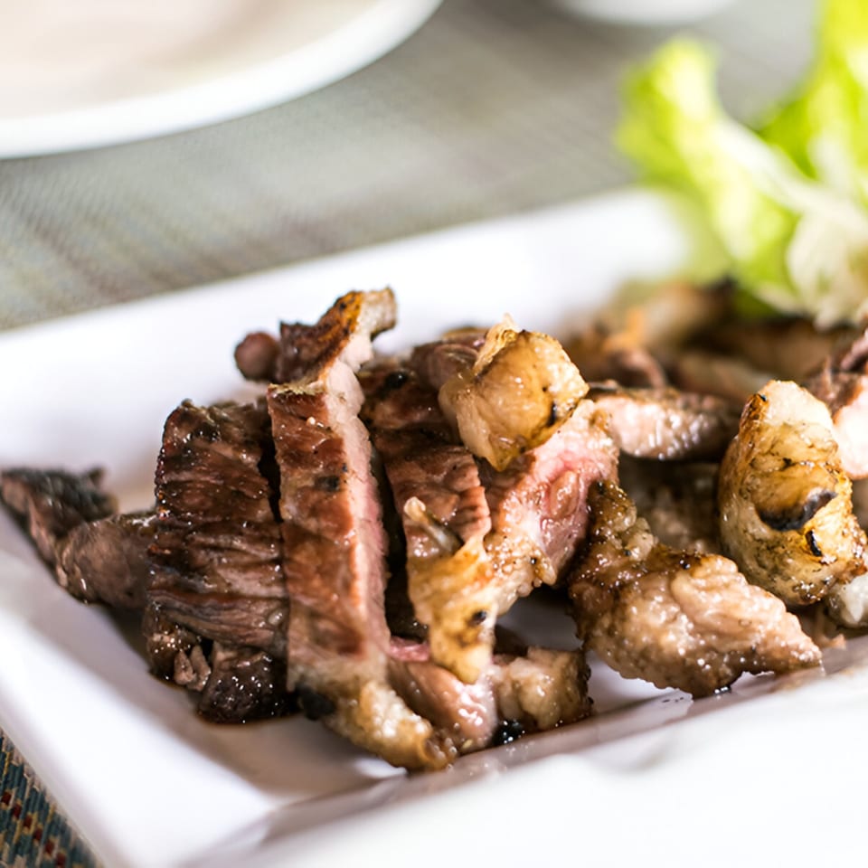 Grilled sliced beef with a pink center and crispy edges, served on a white plate with lettuce.
