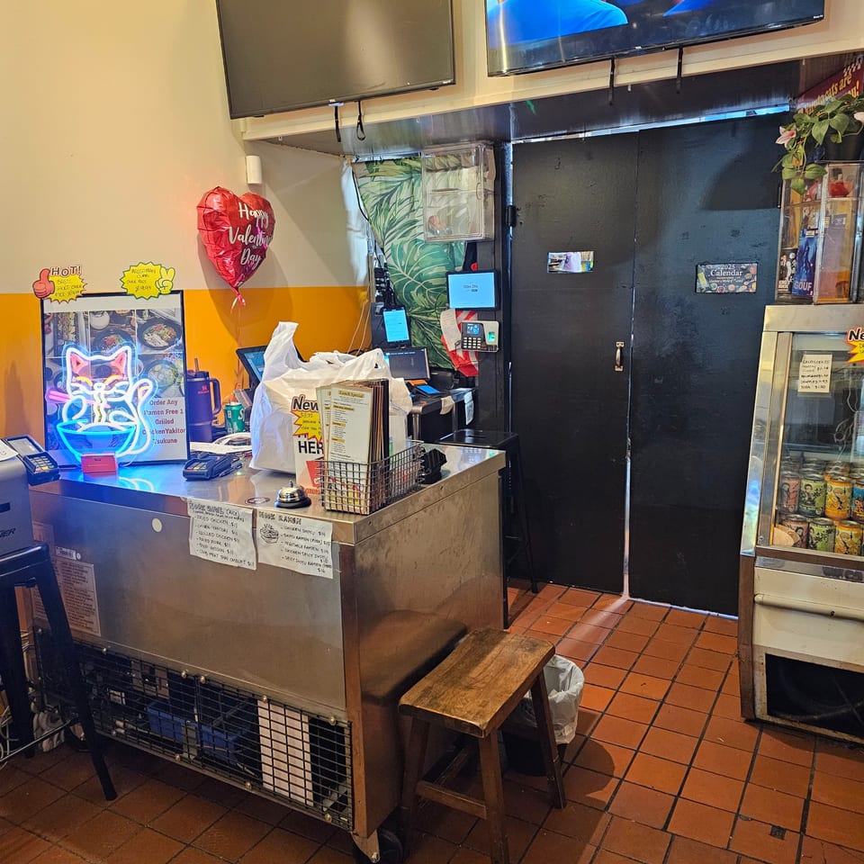 A Thai restaurant's counter with a neon cat sign, menus, and a drink cooler.