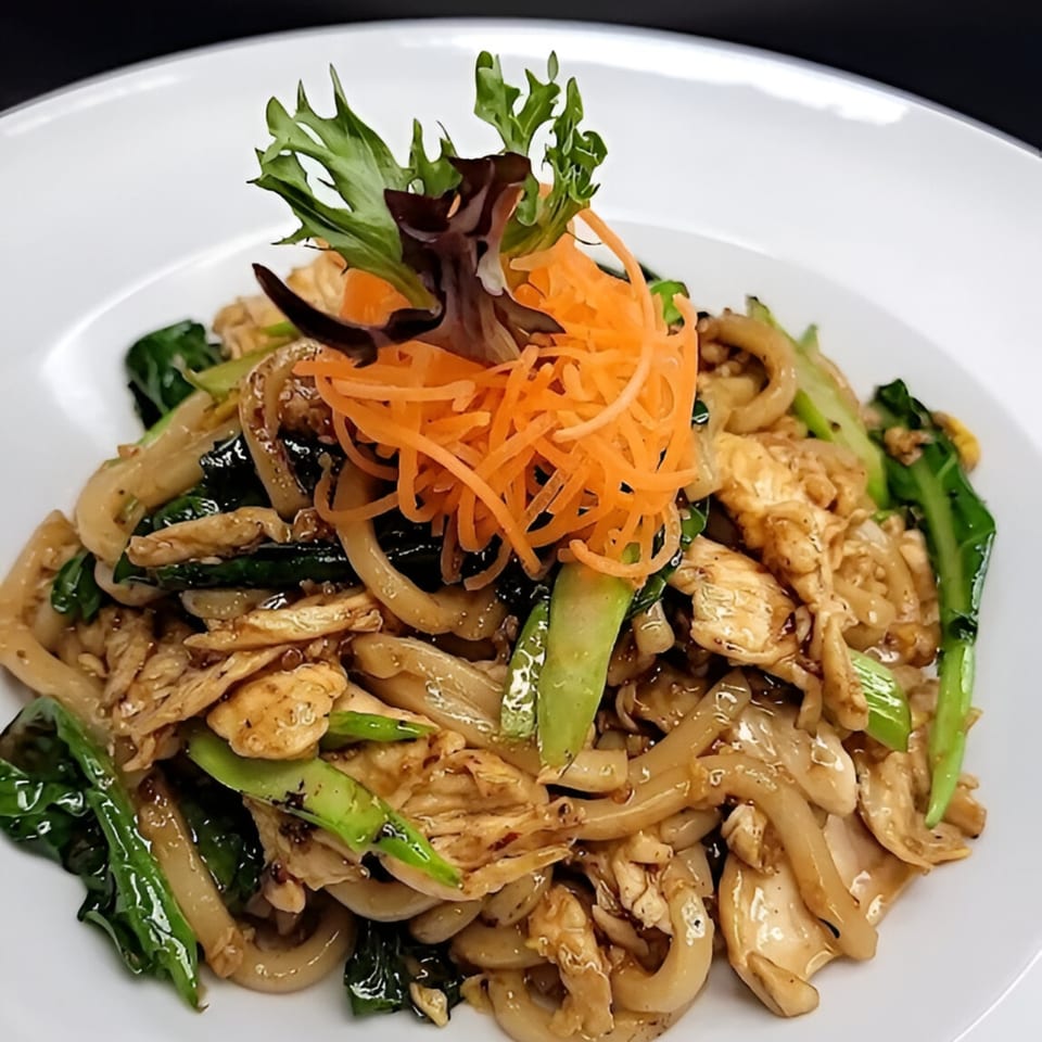 Nook's Thai stir-fried noodles with chicken, green vegetables, and shredded carrots on a white plate.