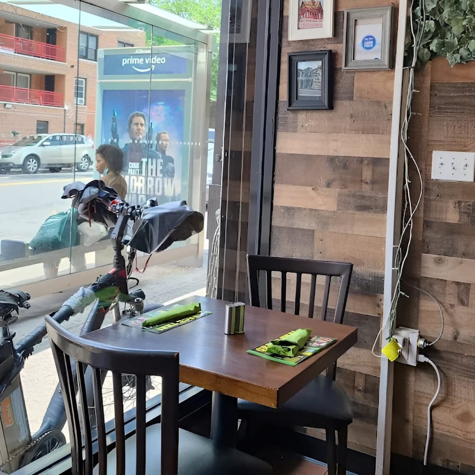 An empty table with green placemats and shakers inside Nook, with a street view outside.