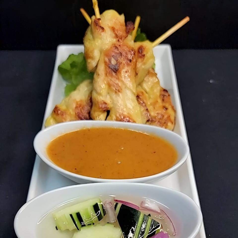 Thai chicken satay skewers with peanut sauce and a cucumber relish on a white platter.