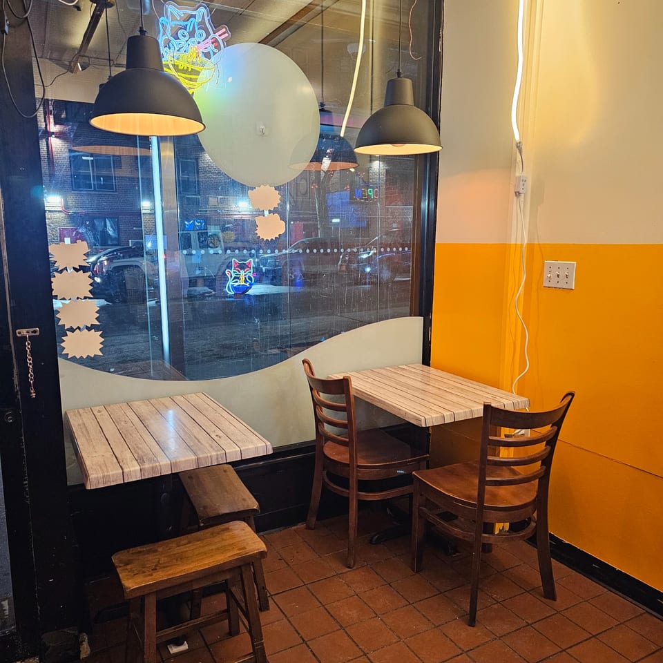 Cozy Nook Thai restaurant interior with small tables, wooden chairs, and a bright yellow wall.