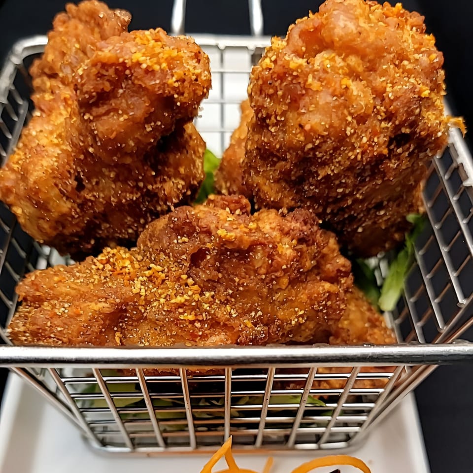 Crispy Thai fried chicken pieces, seasoned with spices, served in a metal basket.